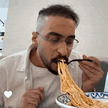 a man wearing glasses is eating noodles with a fork from a bowl