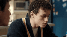 a young man with curly hair is sitting at a table with another young man .