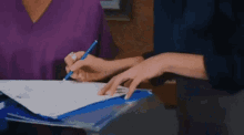a woman is writing on a piece of paper with a pen while sitting at a table .