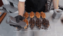 a person pouring chocolate sauce on a tray of waffles