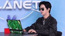 a man wearing sunglasses is typing on a laptop in front of a banner that says planet
