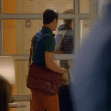 a man in a green shirt is carrying a brown leather bag