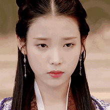 a close up of a woman 's face wearing earrings and a purple dress .