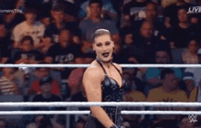 a woman in a black dress is standing in a wrestling ring with a crowd watching .