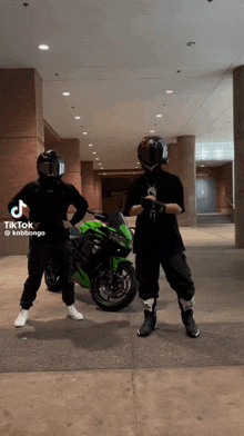 two men wearing helmets are standing in front of a green motorcycle ..