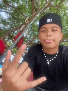 a young man wearing a black hat and a necklace shows his middle finger