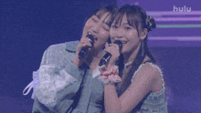 two girls singing into microphones on a stage with the hulu logo in the background
