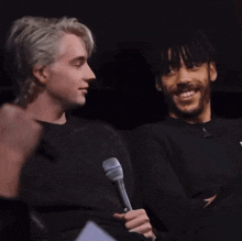 a man holding a microphone next to another man who is smiling