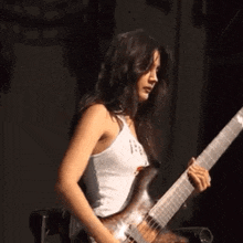 a woman in a white tank top is playing an electric guitar on stage .