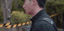 a man wearing a black shirt and tie with a backpack is standing in front of a yellow and black tape .