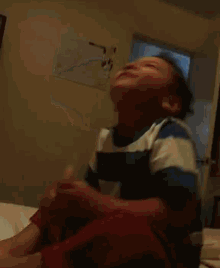 a young boy in a blue and white striped shirt is sitting on a bed holding a bottle of milk