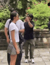 a group of people are standing on a sidewalk in front of a wall .