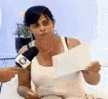 a woman in a white tank top is holding a piece of paper in front of a microphone .