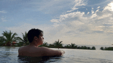 a man is swimming in a pool with palm trees behind him