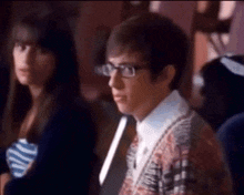 a man wearing glasses is sitting next to a woman in a crowded room .