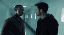 two men are standing next to each other in a hallway and looking at each other .