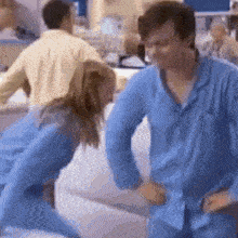 a man and a woman in blue pajamas are dancing on a couch .