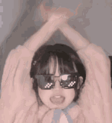 a person wearing sunglasses and a pink sweater is making a heart shape with their hands .