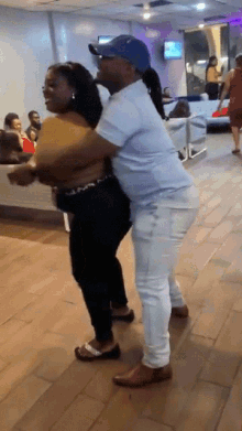 a man in a blue hat is hugging a woman on a wooden floor