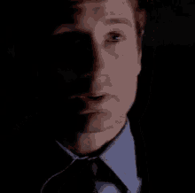 a man in a suit and tie is looking at the camera in a dark room .