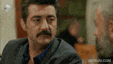 a man with a mustache is sitting at a table with a gifrun.com watermark