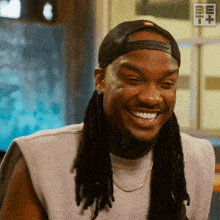 a man with dreadlocks is smiling and wearing a baseball cap and a necklace