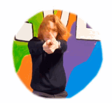 a person pointing at the camera in front of a rainbow colored circle with the word love written on it