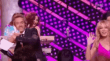 a group of people are dancing on a stage in front of a purple and pink background .