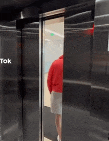 a man in a red sweater is standing in an elevator with the door open .