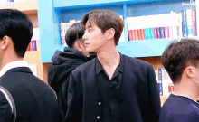 a man in a black jacket stands in front of a bookshelf with the word dear on the bottom