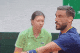 a man in a blue shirt is talking to a woman in a green shirt with a lacoste logo on it