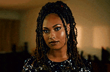 a woman with dreadlocks is wearing a black sequined dress and looking at the camera .