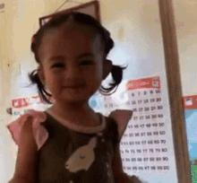 a little girl is standing in front of a calendar that shows the month of october