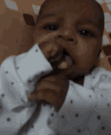 a baby in a white polka dot shirt is sticking out his tongue and making a funny face .