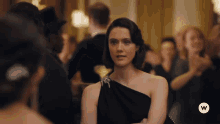 a woman in a black dress stands in a crowd with a white w on the bottom