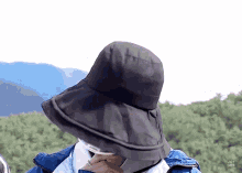 a person wearing a black hat and a blue jacket is covering their face with their hand .