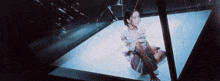 a woman in a white dress is sitting in a room with a broken mirror .