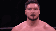 a shirtless man with a beard is standing in a boxing ring looking at the camera .