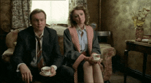 a man and woman sit on a couch holding cups of coffee