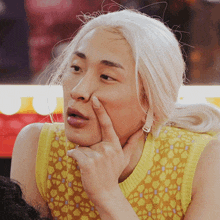 a man with blonde hair is making a funny face with his finger on his nose