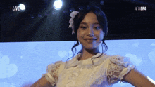a woman in a white lace dress is smiling in front of a blue background that says live