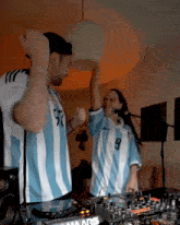 a man and a woman wearing argentina jerseys are dancing in front of a marshall mixer