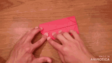 a person is folding a piece of red paper on a wooden table and the words made in animatica are visible
