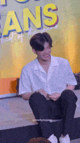 a man sits in front of a sign that says fans