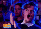 a man is clapping in a crowd with a today darwin 32 sign in the background .