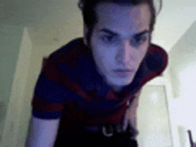a man in a blue and red striped shirt is standing in a room and looking at the camera .