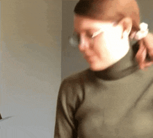 a woman wearing a turtleneck and glasses is holding her hair .