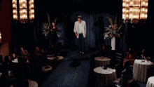 a man in a white jacket is dancing in a dark room with people sitting at tables