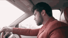 a man in a red suit is driving a car and looking out the window .
