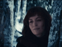 a woman is leaning against a tree in the woods .